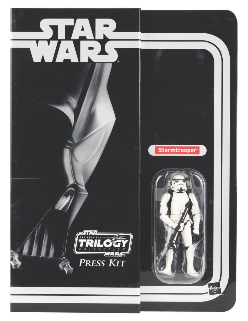 A Hasbro Star Wars Original Trilogy Toy Fair Press Kit.: (Hasbro, 2004) A Star Wars original trilogy toy fair press kit with an unopened Stormtrooper action figure. The Stormtrooper holds a large black rifle and has poseable arms and legs. The press kit’s