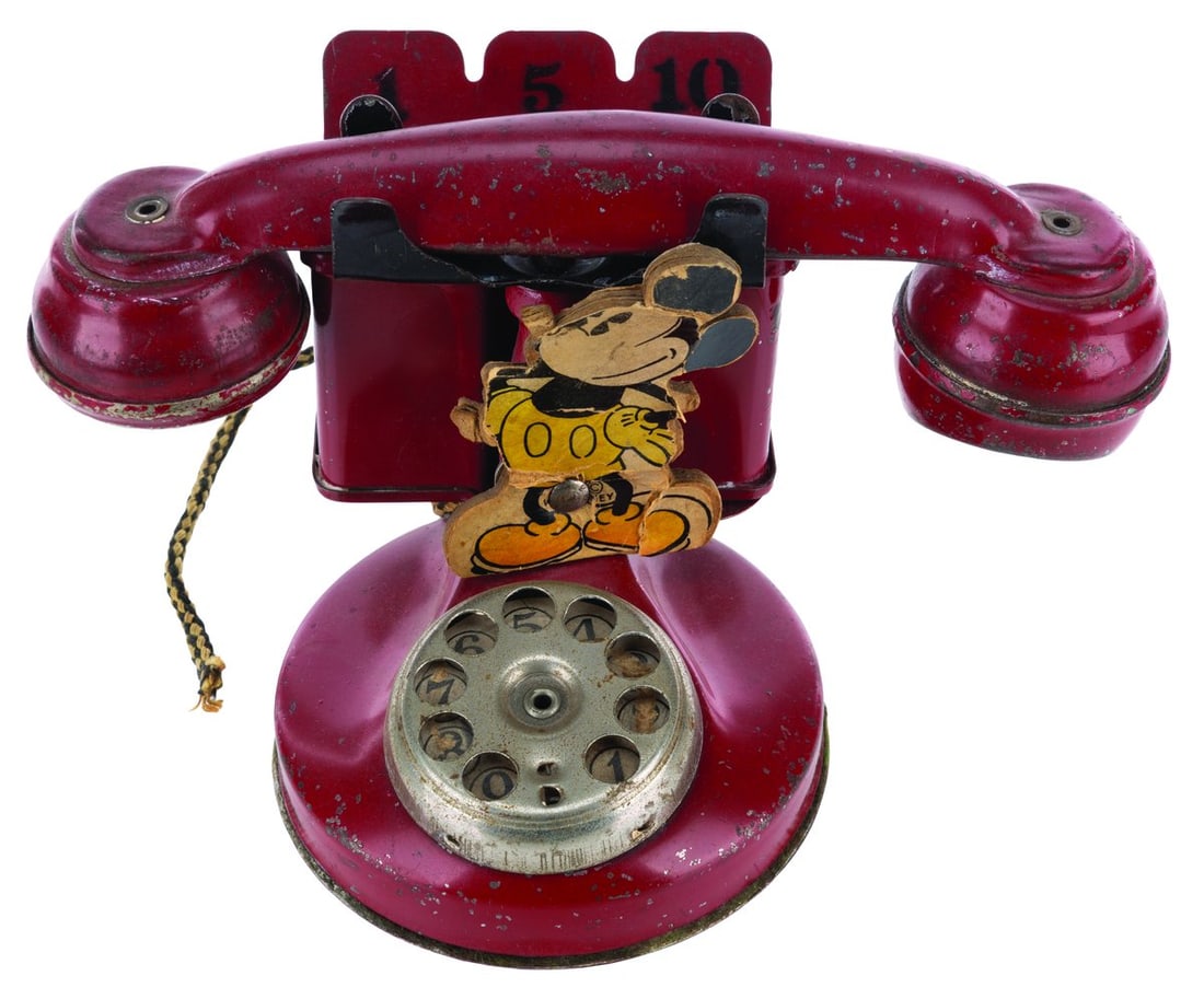 A Mickey Mouse Telephone with Coin Bank Toy.: (N.N. Hill Brass Co., 1930s) An early children’s metal Mickey Mouse rotary telephone toy with an attached coin bank. When the rotary dial is used, a bell rings. Measuring 5.5" x 8.5" x 4.5" tall, th