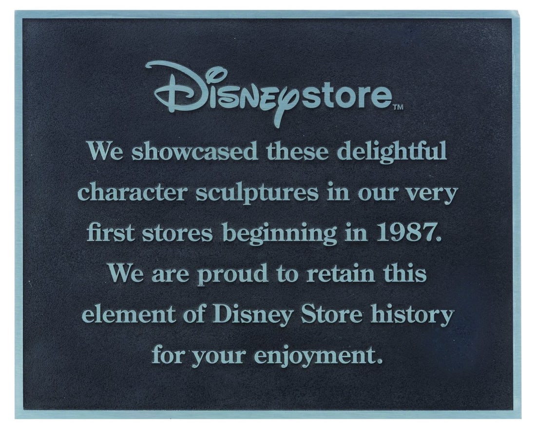 A Disney Store Commemorative Plaque.: (Disney, 2000s) A metal sign commemorating the original Disney character display figures that remain an essential part of the Disney Store experience. A major presence in malls from the late 1980s thr