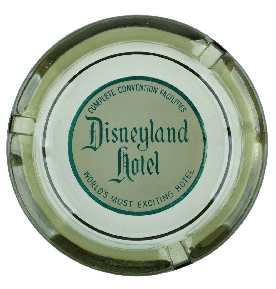 An Early Disneyland Hotel Ashtray.: (Disneyland Hotel, 1960s) An elegant early smoked glass ashtray from the Disneyland Hotel. The well features the hotel logo and tagline "The World's Most Exciting Hotel," with "Complete Convention Fac