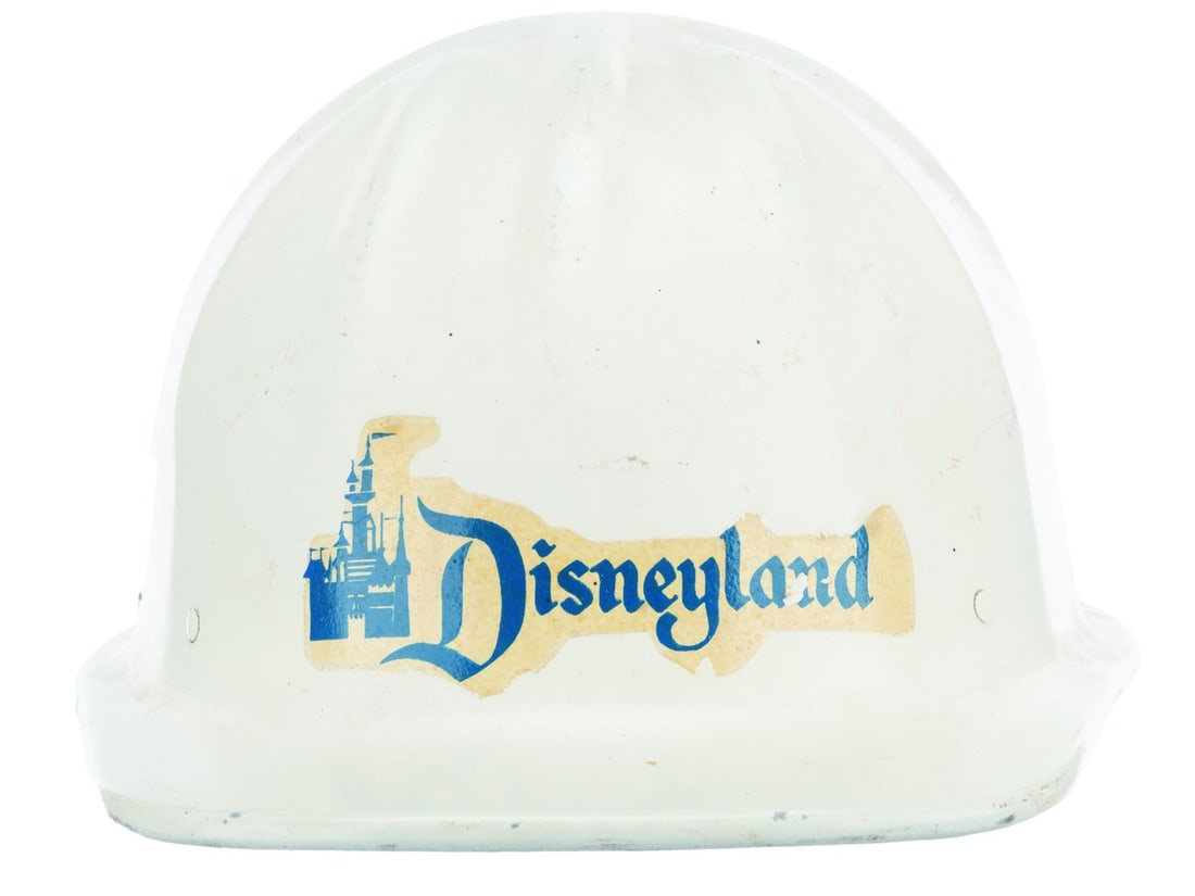 A 1960s Disneyland Construction Hard Hat.: (Disneyland, 1960s) A construction hard hat from the early days of Disneyland. Unlabeled, the hard hat is in good condition with typical scuffs, discoloration from age, sticker loss, and wear from use
