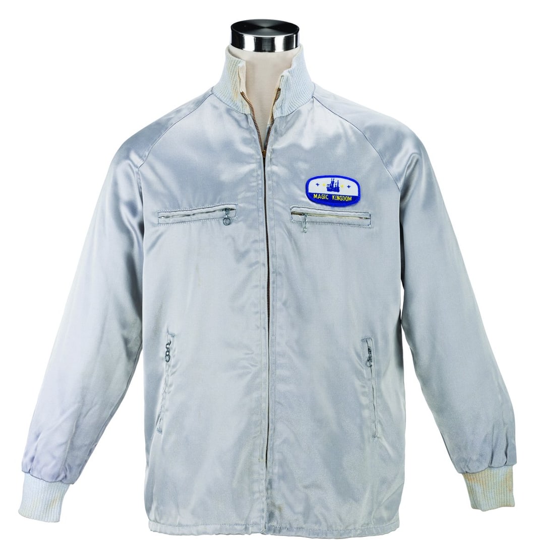 A Magic Kingdom Silver Cast Member Jacket.: (Walt Disney World, 1970s-90s) A silver jacket worn by Cast Members working at the Magic Kingdom. Labeled a size L, the jacket displays in good condition with light wear and heavy stains on the collar