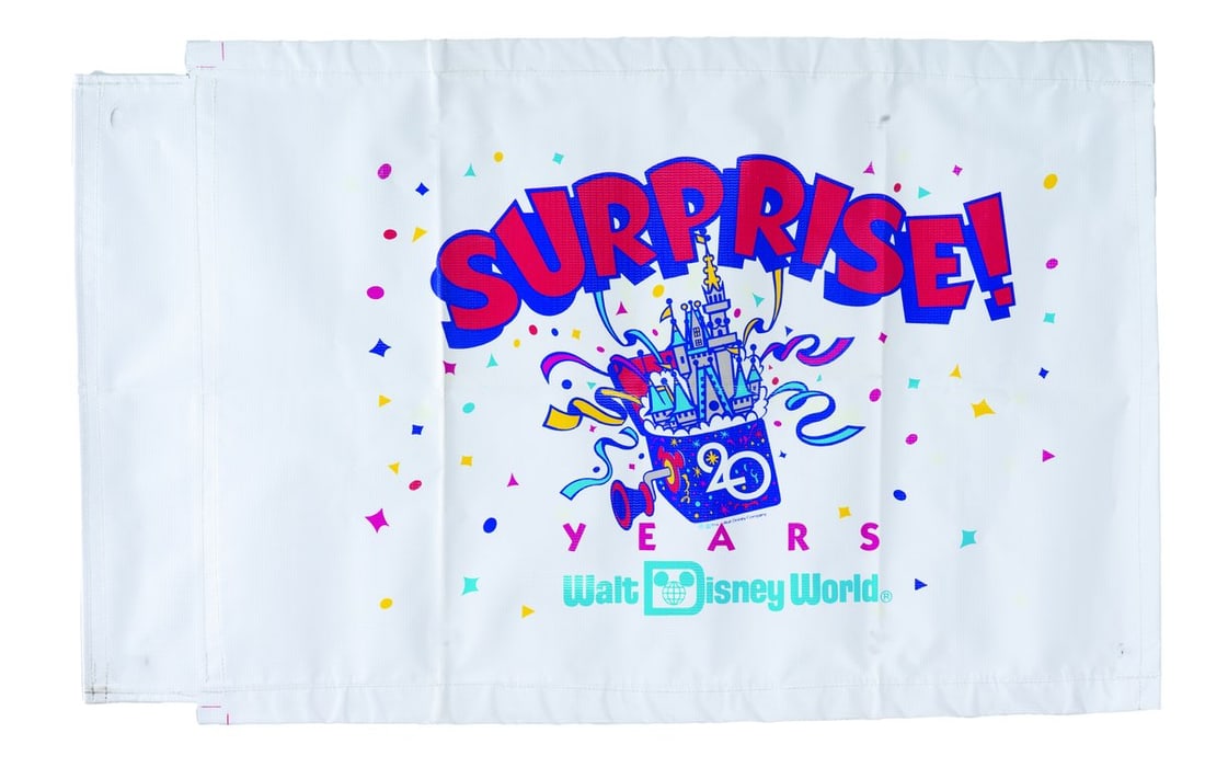 A Walt Disney World 20th Anniversary Banner.: (Walt Disney World, 1991) A double-sided Surprise banner from Walt Disney World's 20th anniversary celebration. Measuring 25.75" x 36", the banner is in very good condition with light wear and blue ma