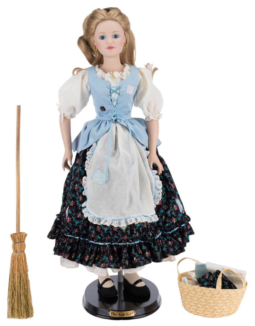 A "Cinderella The Ash Girl" Doll.: (Danbury Mint, 1987) A "Cinderella The Ash Girl" porcelain doll with a straw basket of linen, broom, and wooden display stand. Measuring 25" tall, the doll is in fine condition with the original box.
