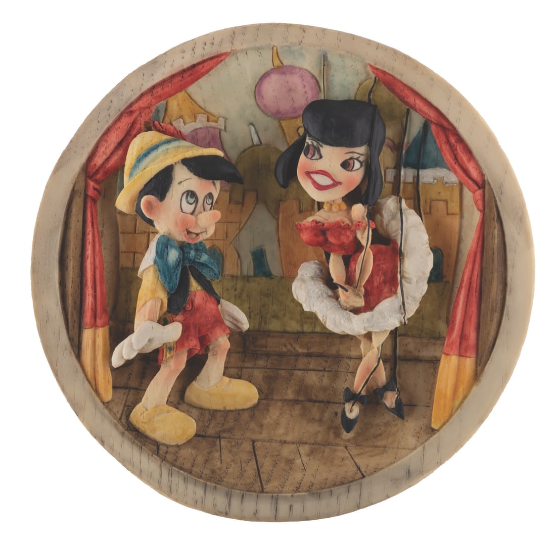 A "Pinocchio" and Marionette 3-D Relief Plate.: (Disney, 1999) A "Pinocchio" decorative plate produced in Italy featuring a relief of Pinocchio and a French dancer marionette. The heavy resin plate is cast from a hand-carved wooden original sculpte