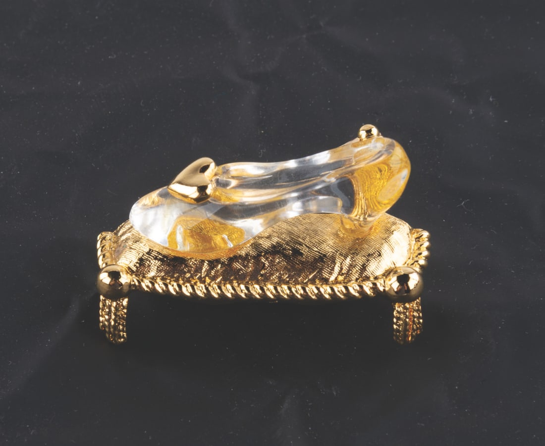A "Cinderella" Glass Slipper Brooch.: (Napier, 2000s) A "Cinderella" glass slipper brooch with a gold-colored heart and pillow, manufactured by Napier. The brooch comes with its original box and is in very good condition with a tiny spot