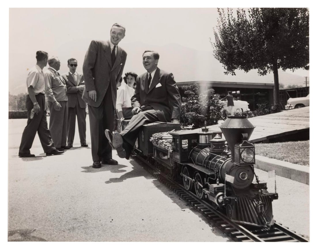 A Walt Disney Lilly Belle Train Publicity Photo.: (Disney, 1951) A publicity photo of Walt Disney aboard his 1:8 scale replica train on the Walt Disney Studios backlot. Featured are the Lilly Belle engine, film director Robert Florey, and a group of 