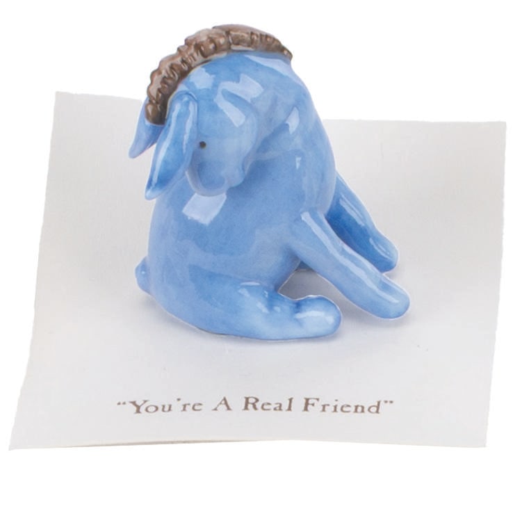 A Mini "Winnie the Pooh" Eeyore Figurine.: (Michel and Co., 1990s) A mini ceramic figurine of Eeyore, inspired by the original illustrations for the Winnie the Pooh books by E. H. Shepard. The figurine is attached to a card with a quote that