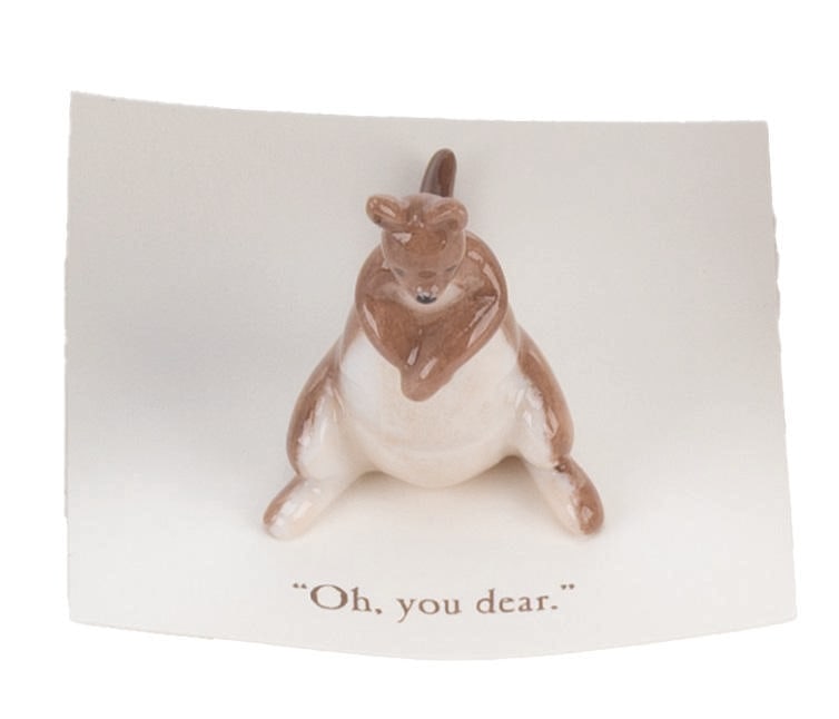 A Mini "Winnie the Pooh" Kanga Figurine.: (Michel and Co., 1990s) A mini ceramic figurine of Kanga, inspired by the original illustrations for the Winnie the Pooh books by E. H. Shepard. The figurine is attached to a card with a quote that