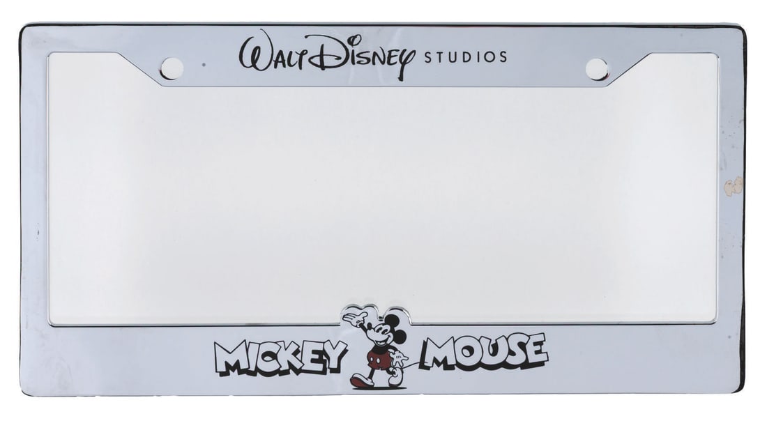 A Walt Disney Studios License Plate Frame.: (Disney, 2000s) A Walt Disney Studios license plate frame featuring Mickey Mouse. Measuring 6.25" x 12", the chrome metal license plate frame is in very good, unused condition with a small spot of