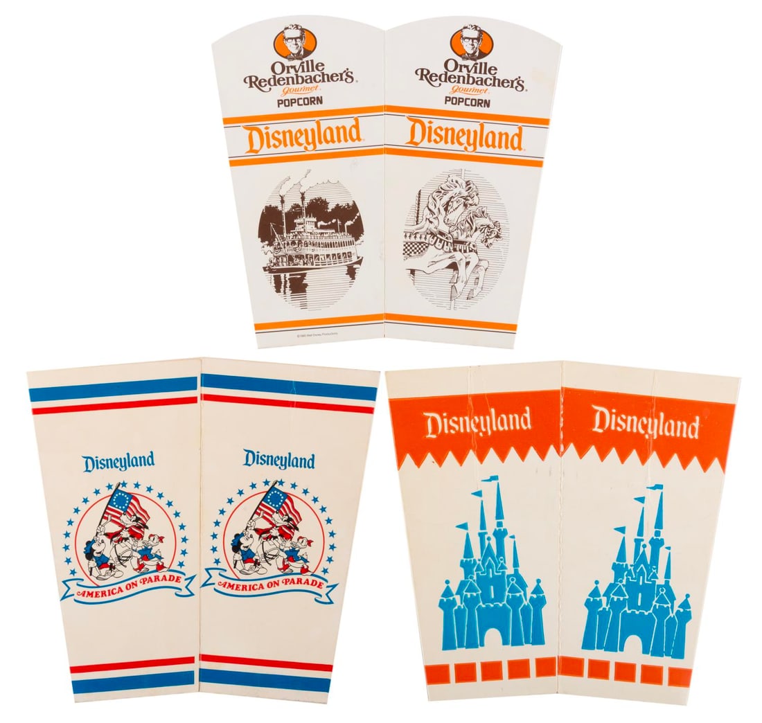 A Trio of Disneyland Popcorn Buckets.: (Disneyland, 1970s-80s) Three cardboard popcorn buckets from Disneyland featuring America on Parade, Sleeping Beauty Castle and Orville Redenbacher with Disneyland icons. Measuring 6" x 7" folded