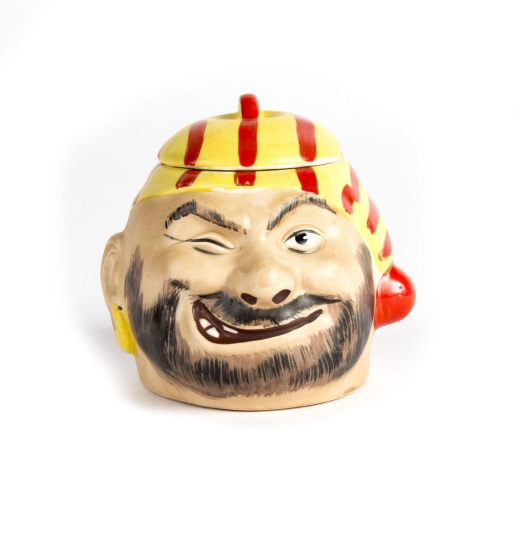A Pirates of the Caribbean Souvenir Condiment Jar.: (Disneyland, 1967) A hand-painted ceramic condiment jar themed after Disneyland's Pirates of the Caribbean attraction. This jar depicts a pirate character and has a removable lid for use as a condimen