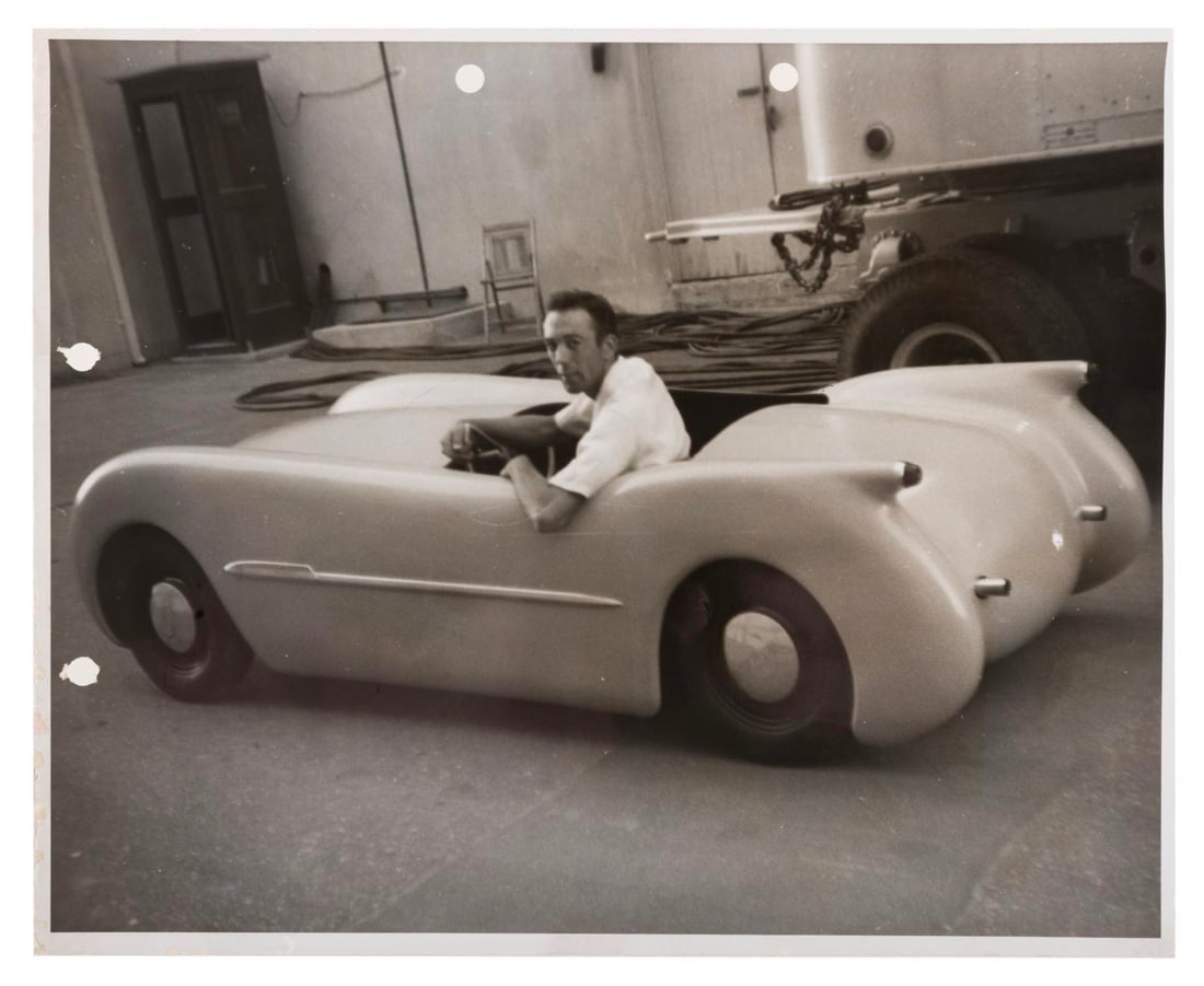 An Early Autopia Prototype Vehicle Photo.: (Disneyland, 1950s) A photo of an early prototype Autopia ride vehicle with an unknown Imagineer, two edges punched, most likely to include in a production reference set of photos. Measuring 8" x 10",
