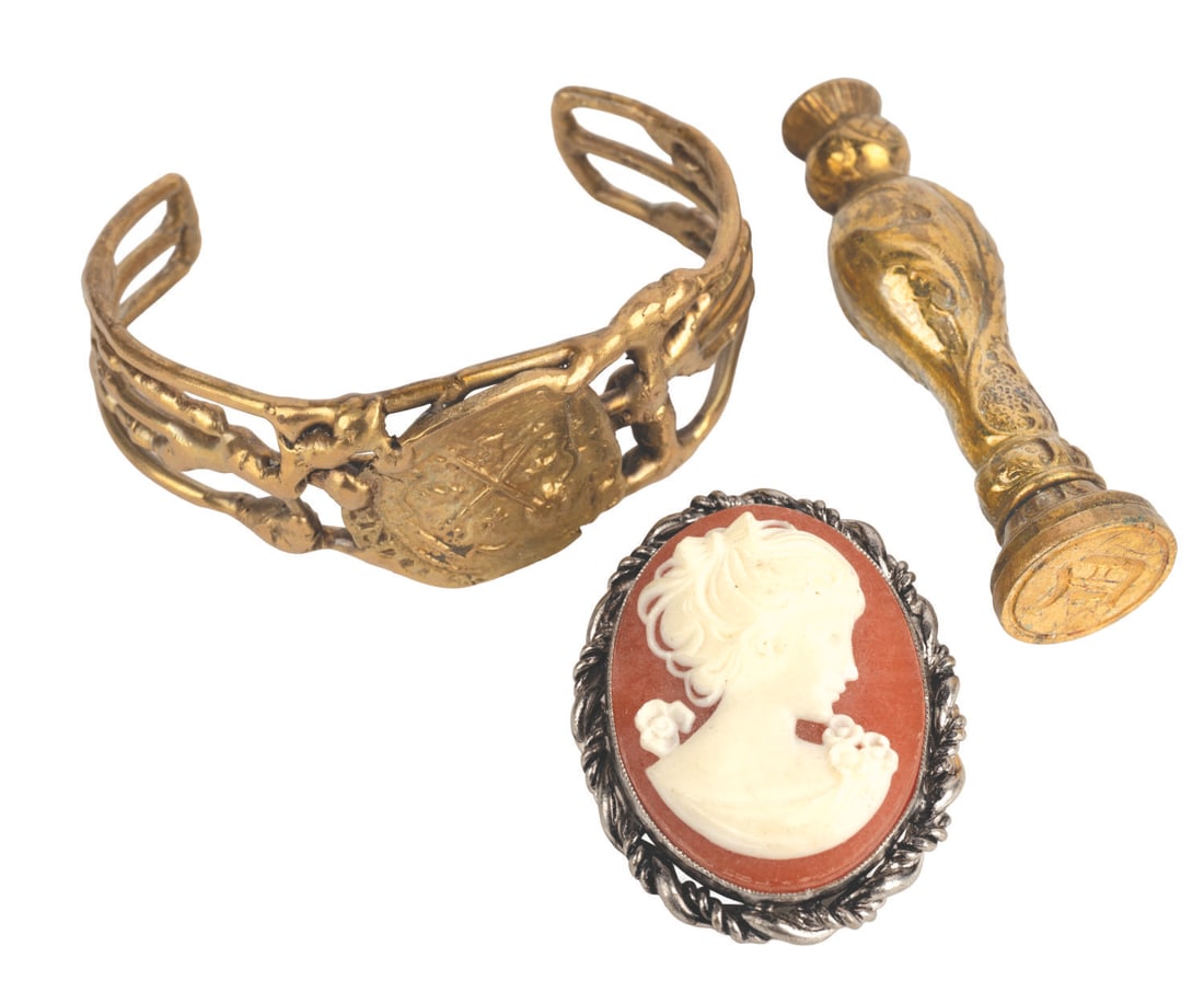 One-Eyed Willy Treasure Props from "The Goonies.": (Warner Bros., 1985) Three "The Goonies" props from One-Eyed Willy's vast treasure hoard. Included are a cameo brooch, a gold bracelet, and a brass wax seal stamp. Measuring 1.5" x 2" to 2" x 2.5",