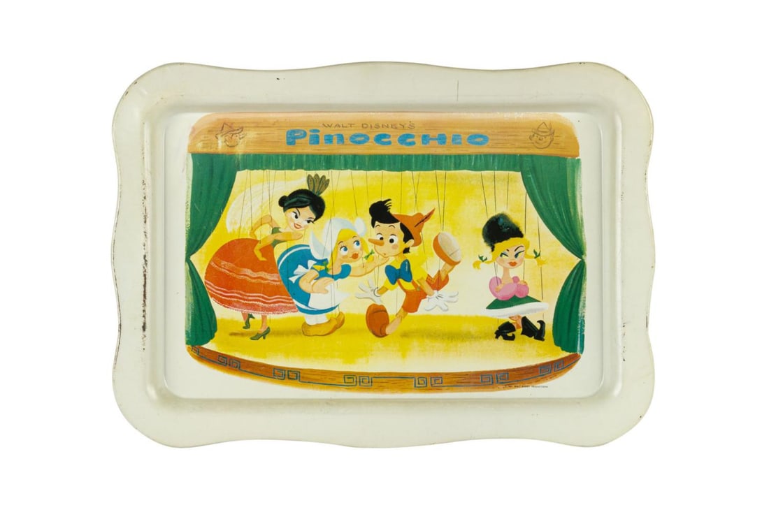 A 1960s "Walt Disney's Pinocchio" Tin Tray.: (Disney, 1961) A Walt Disney’s Pinocchio tin tray featuring Pinocchio surrounded by three of Stromboli’s dancer puppets. Measuring 12.75” x 17.75”, the tray displays in good condition