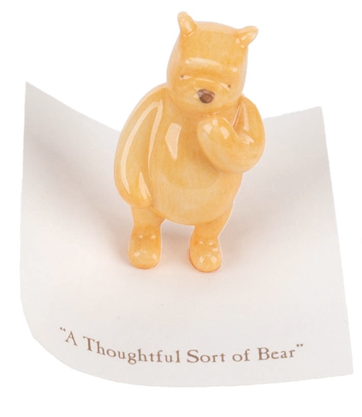 A Michel and Co. Winnie the Pooh Mini Figure.: (Michel and Co., 1990s) A mini ceramic figurine of Winnie the Pooh, inspired by the original illustrations for the books by E. H. Shepard. The figure is attached to a card with a quote that reads "A T