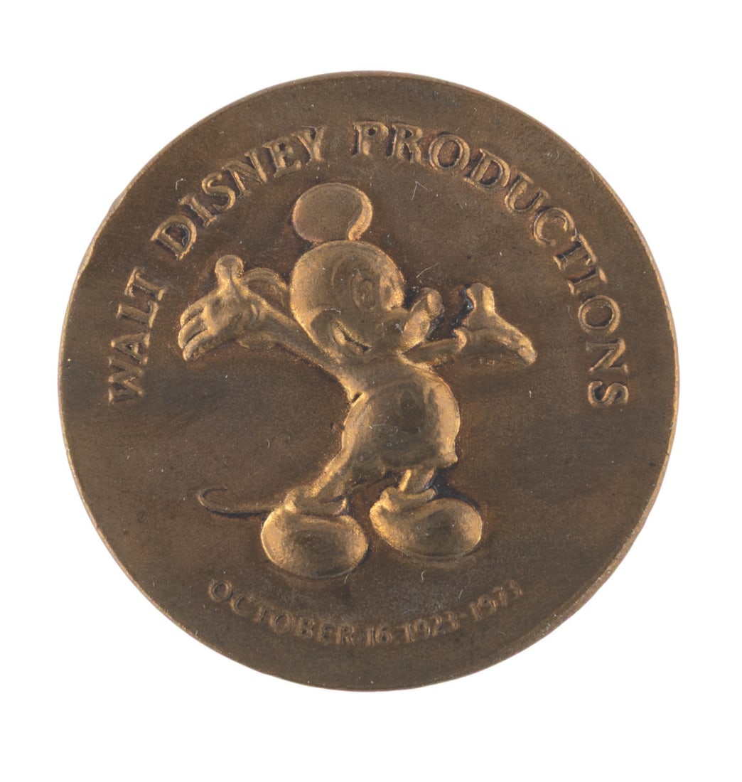 A Walt Disney Productions 50th Anniversary Coin.: (Disney, 1973) A coin commemorating Walt Disney Productions? 50th anniversary featuring Mickey Mouse on the front and a quote from Walt on the reverse. Measuring 1.5" in diameter, the medallion is in
