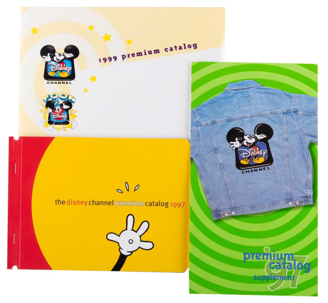 A Pair of 1990s Disney Channel Premium Catalogs.: (Disney Channel, 1997/99) A pair of catalogs presenting premium items (swag) available to promote the Disney Channel in 1997 and 1999. The catalogs are in fine condition, with the 1999 catalog sealed.