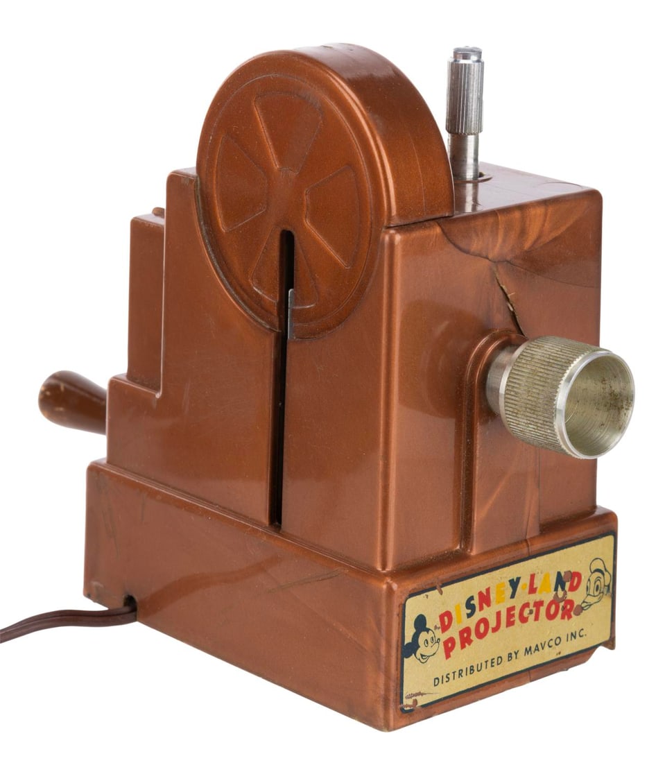 A 1955 Mavco Disneyland Projector Toy in Original Box.: (Mavco, 1955) An early “Disney-land” projector toy, with the original box. Measuring 7.25” x 2.75” x 5” tall, the toy displays in fair condition with a crack in the front,