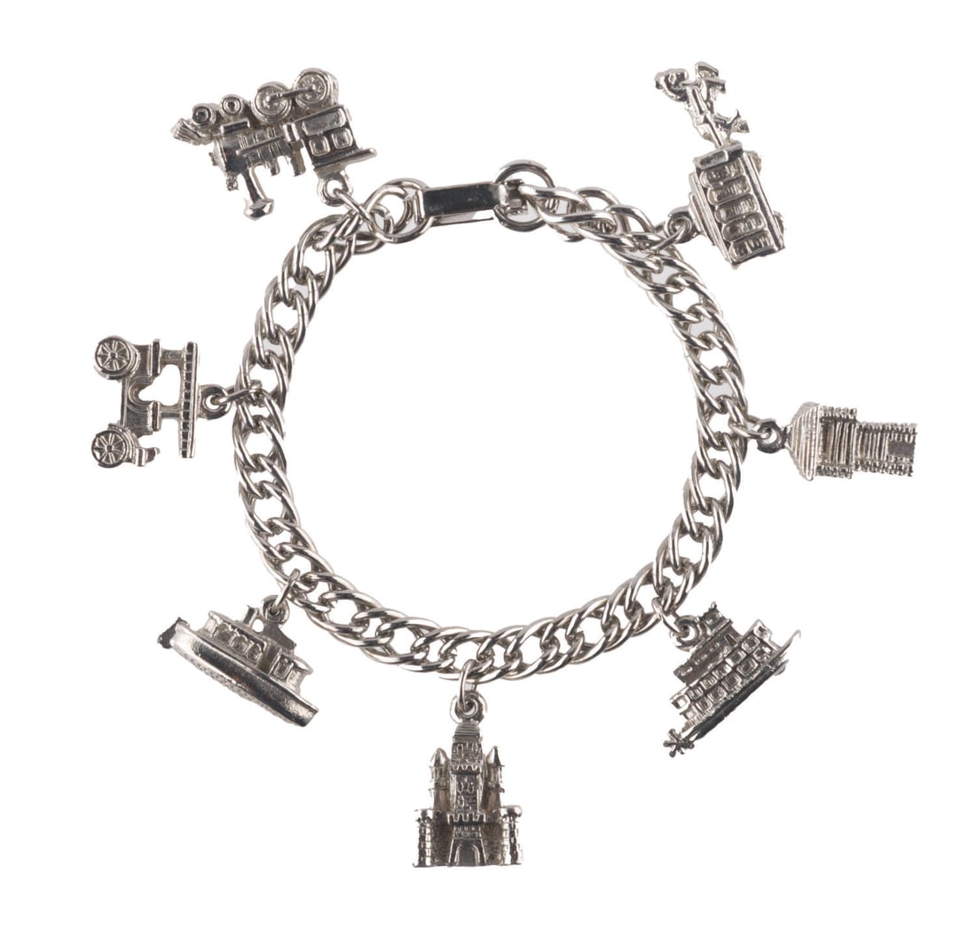 A Disneyland Attractions Charm Bracelet.: (Disneyland, 1950s-60s) A silver-toned souvenir charm bracelet from Disneyland featuring seven charms based on Park attractions. Included are a train car, a Main Street jitney, a Jungle Cruise boat,