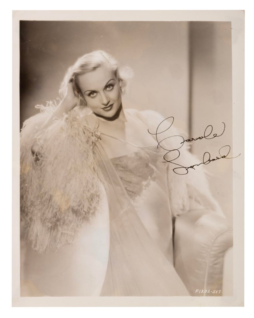 A Carole Lombard Signed Photograph.: (Lombard, 1930s) A photograph of actress Carole Lombard, with a signature most likely from a Studio secretary. Measuring 8" x 10", the photo is in very good condition with light handling wear,