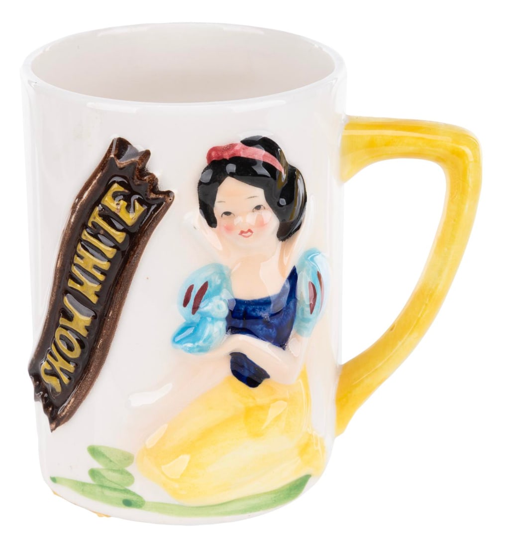 A 1960s Snow White Mug.: (Enesco, 1960s) A ceramic mug with a 3D relief of Snow White. Measuring 3.75" tall and 2.75" in diameter, the mug displays in good condition with spots of discoloration, scuffs, adhesive residue on