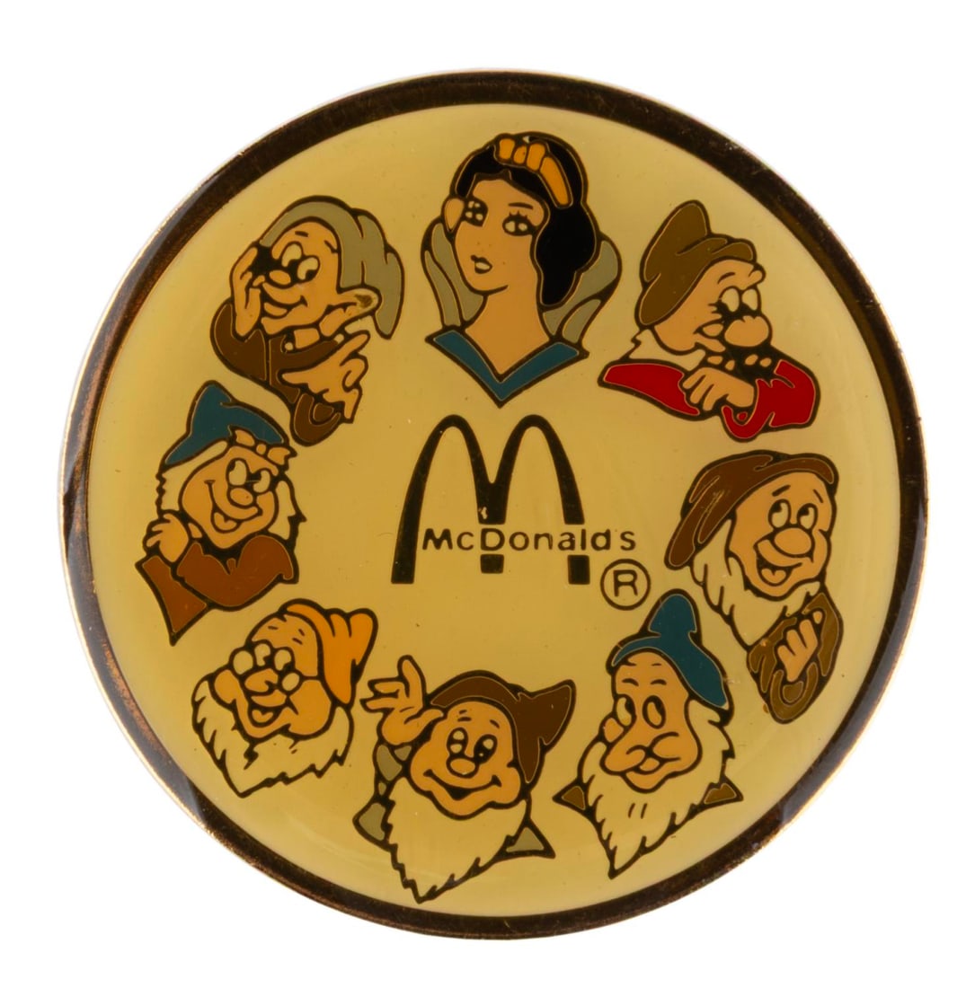 A McDonald's "Snow White and the Seven Dwarfs" Pin.: (McDonald's, 1980s) A promotional "Snow White and the Seven Dwarfs" pin from McDonald's. Measuring 1.5" across, the pin is in very good condition with discoloration to the enamel and light scuffs and