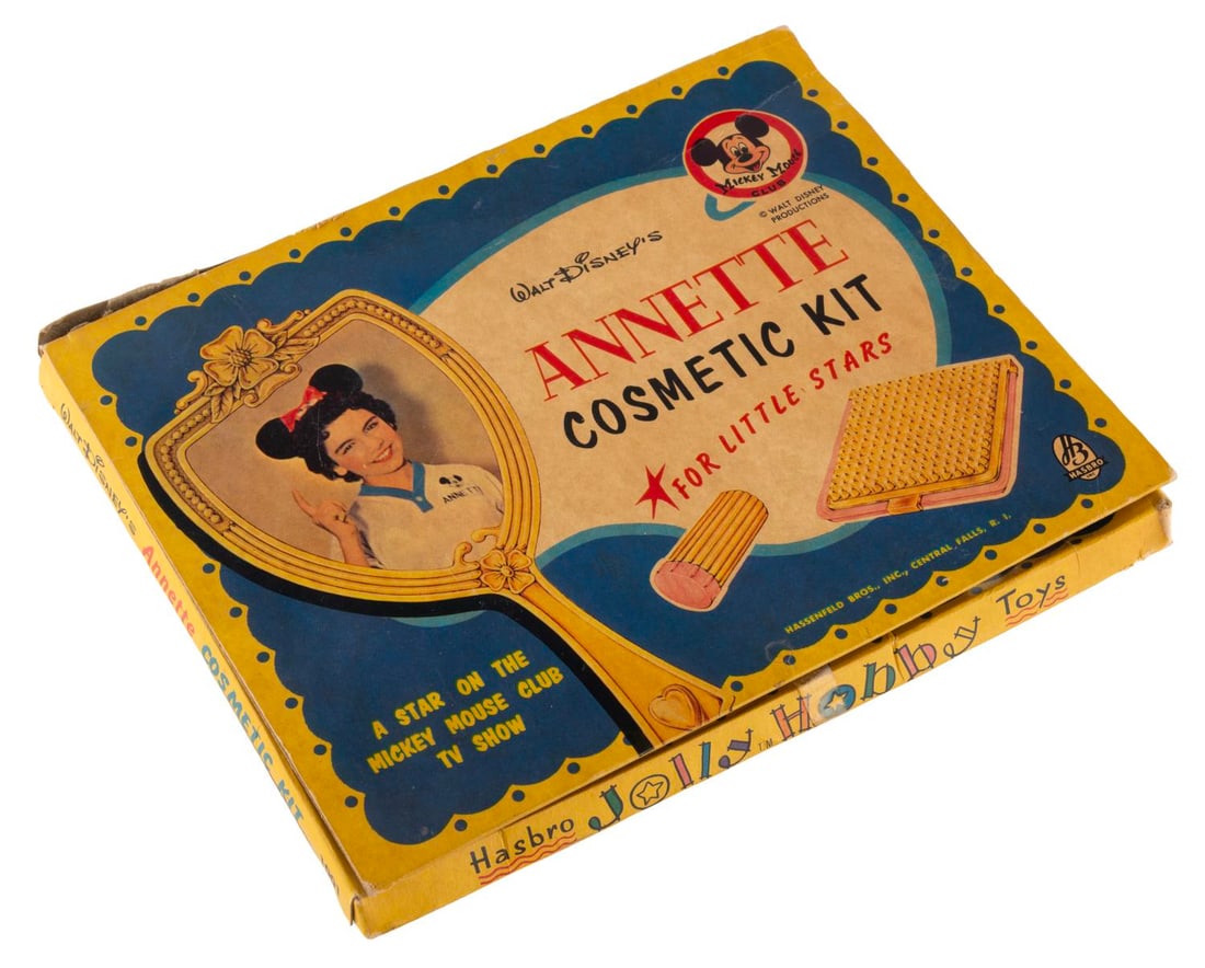 A Mickey Mouse Club Annette Toy Cosmetic Kit.: (Hasbro, 1950s) A Mickey Mouse Club Annette toy cosmetics kit, including three of the original eight toy cosmetics: an emery board, lipstick, and a powder compact. Measuring 5" x 9", the kit is in goo