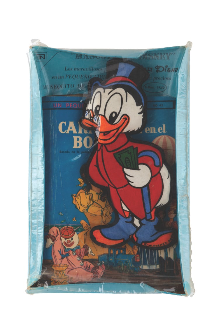 A Mexican "Babes in Toyland" Book and Scrooge McDuck Figure.: (Disney, 1960s) A Mexican "Babes in Toyland" book and a Scrooge McDuck stuffed figure in their original packaging. Measuring 7" tall in its 6.5" x 10" packaging, the doll and book are in presumed very