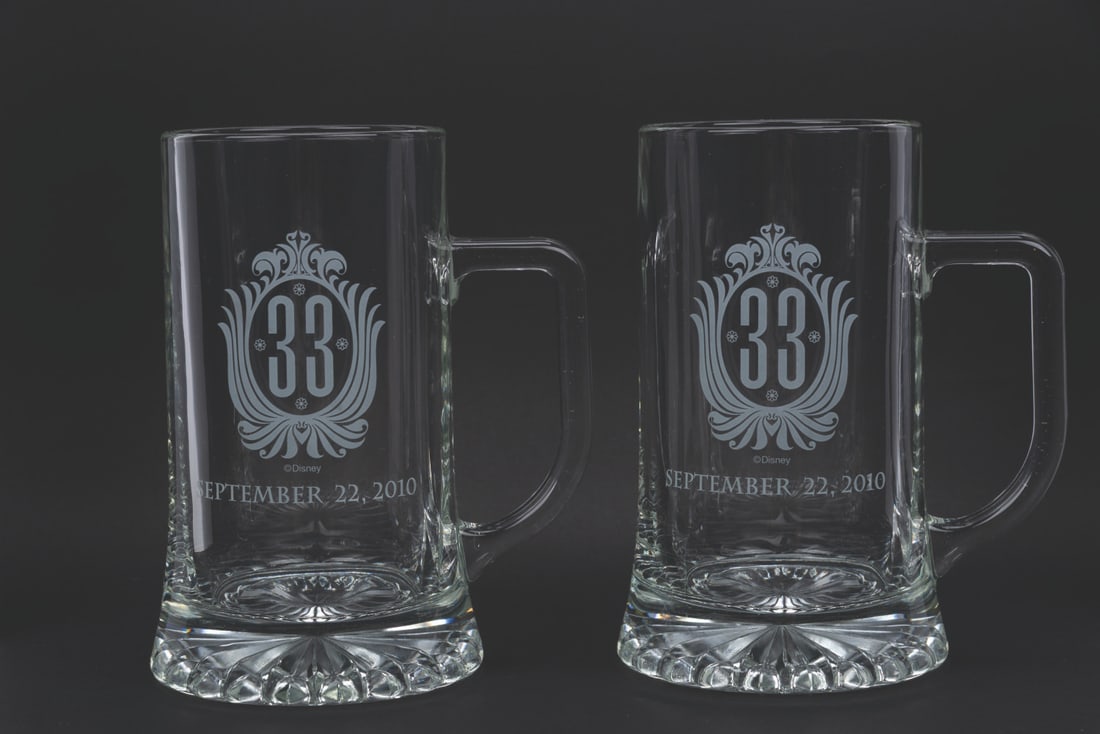 A Pair of Club 33 Oktoberfest 2010 Mugs.: (Disneyland, 2010) A pair of etched mugs from Club 33's Oktoberfest event on September 22, 2010. Measuring 6.25" tall each and 3.75" in diameter, the mugs display in very good condition with light wea