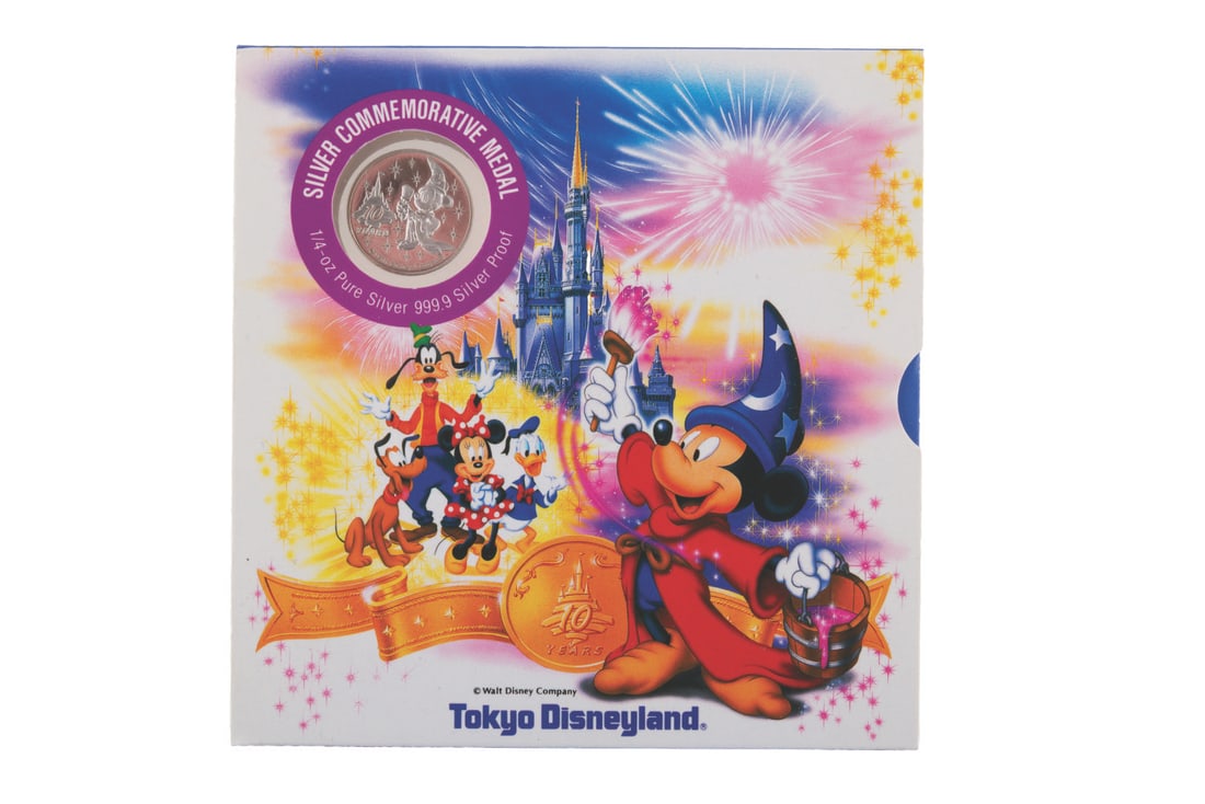 A Tokyo Disneyland 10th Anniversary Silver Coin.: (Tokyo Disneyland, 1993) A pure silver coin commemorating the 10th anniversary of Tokyo Disneyland. Measuring 1" in diameter in its 5.25" x 5.25" sleeve, the coin is in fine condition, while the