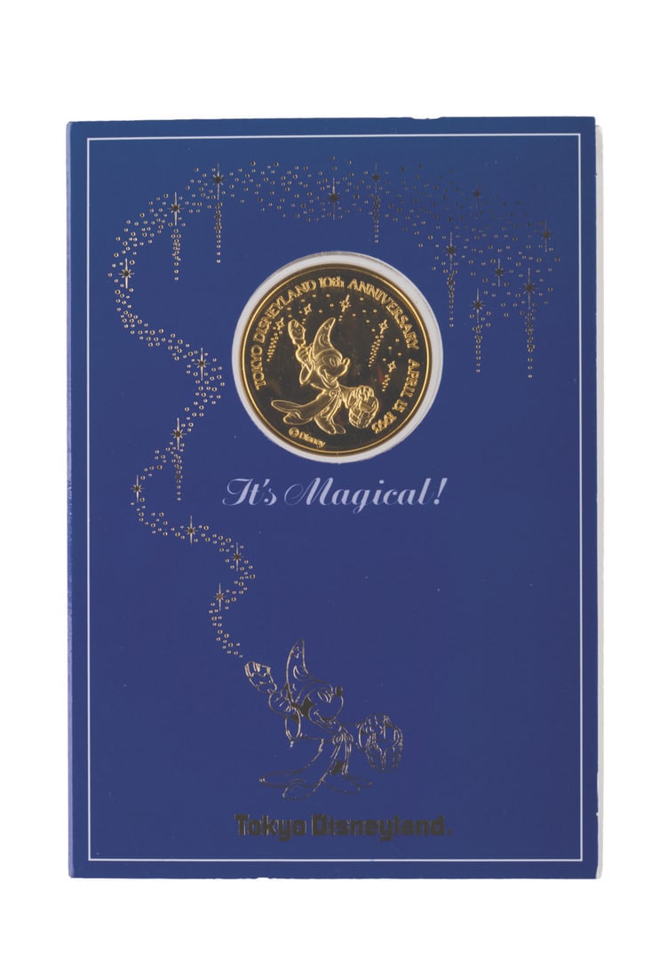 A Tokyo Disneyland 10th Anniversary Gold Coin.: (Tokyo Disneyland, 1993) A gold coin commemorating the 10th anniversary of Tokyo Disneyland, dated April 15, 1993. Measuring 1.5" in diameter in its 4.25" x 6.25" sleeve, the coin is in fine