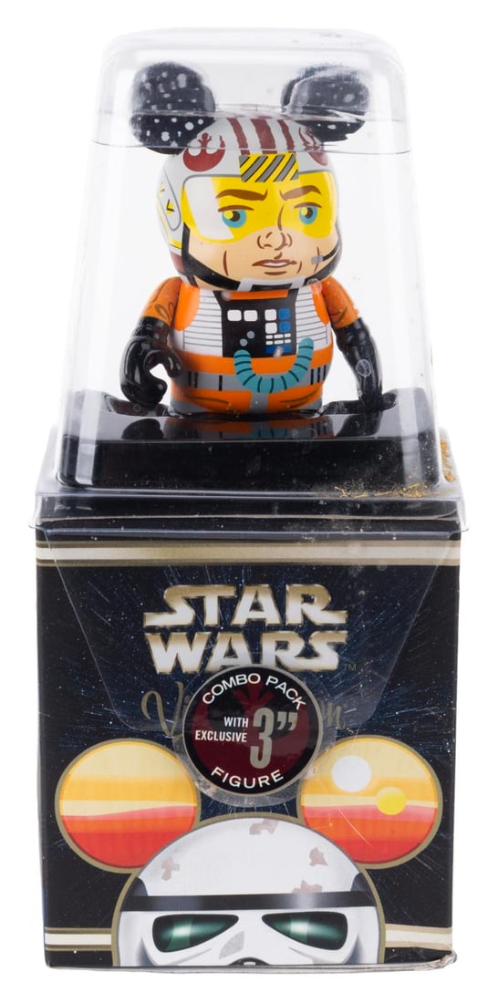 A Vinylmation Lukle Skywalker X-Wing Pilot Figurine.: (Disney, 2010s) A Luke Skywalker X-Wing Pilot Vinylmation blind box figurine. Measuring 3" tall, the figurine is in fine condition, while the packaging exhibits discoloration and wear.