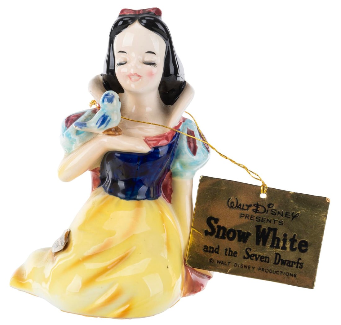 A "Snow White and the Seven Dwarfs" Ceramic Bank.: (Enesco, 1960s) A figural ceramic savings bank of Snow White with a blue bird. Measuring 4.75" tall, the bank is in very good condition with light soiling and adhesive on the base from previous displa