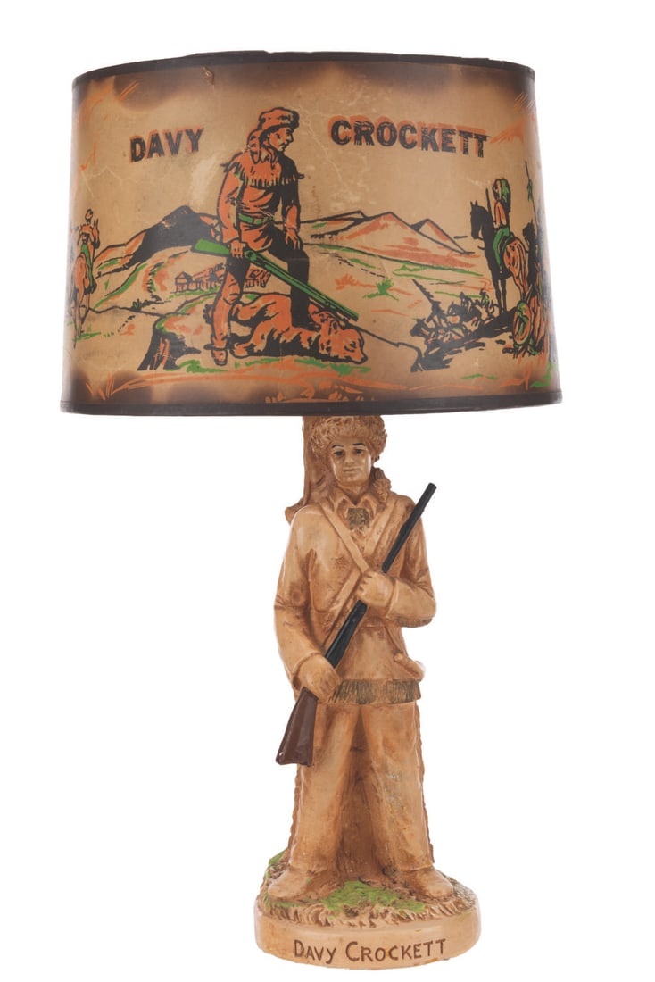 A Davy Crockett Lamp with Shade.: (Premco Mfg., 1955) A Davy Crockett chalkware lamp with shade. The figure of Crockett supports a functioning lamp, with the rare shade that depicts him in the wilderness. Measuring 9" diameter x 14.25