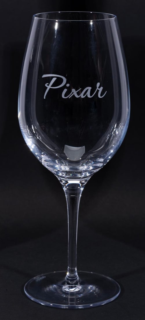 A Pixar Wine Glass.: (2000s) A wine glass with "Pixar" on the front. Measuring 9" tall and 3" in diameter, the wine glass is in very good condition with light wear.
