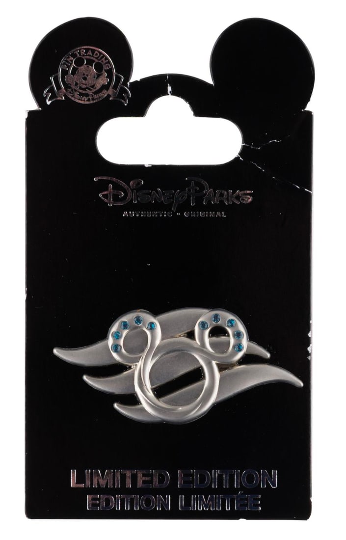 A Disney Cruise Line Limited Edition Pin.: (Disney Cruise Line, 2012) A pin of the Disney Cruise Line logo with blue "jewel" elements, released in a limited edition of 1000. The pin is in very good condition.