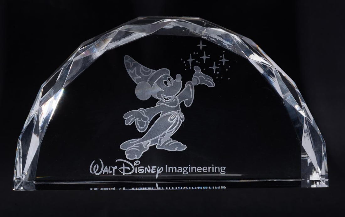 A Walt Disney Imagineering Paperweight.: (Walt Disney Imagineering, 2012-19) A heavy paperweight featuring the logo for Walt Disney Imagineering. Measuring 6" x 1.75" x 3.25" tall, the crystal paperweight comes with its original box and is i