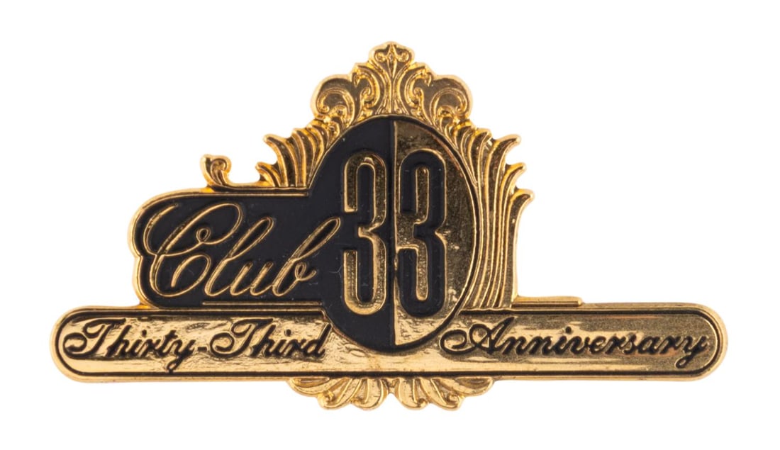 A Club 33 Thirty-Third Anniversary Lapel Pin.: (Disneyland, 2000) A gold-toned pin commemorating the thirty-third anniversary of Disneyland's exclusive Club 33. Measuring 1.75" wide the pin is in very good condition.