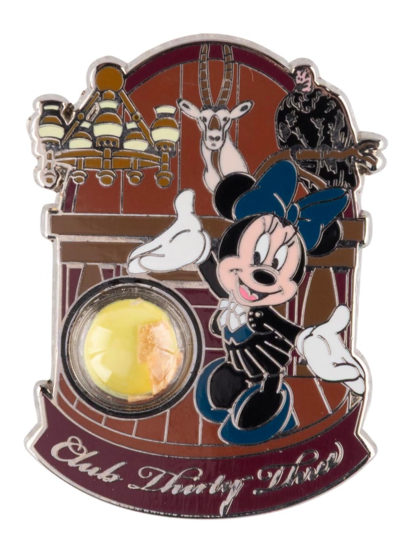 A Club 33 "Piece of History" Pin.: (Disneyland, 2015) A Club 33 "Piece of History" pin. Depicting Minnie Mouse in the original trophy-lined dining room, the pin contains pieces of the cypress wood paneling removed from the Club during 