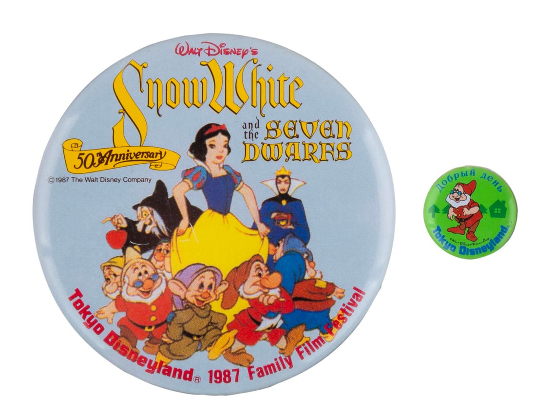 A Pair of Tokyo Disneyland "Snow White" Buttons.: (Tokyo Disneyland, 1980s) A pair of early Tokyo Disneyland buttons themed to "Snow White and the Seven Dwarfs." Included are a 1987 Film Festival button and an unusual button of Doc with Russian