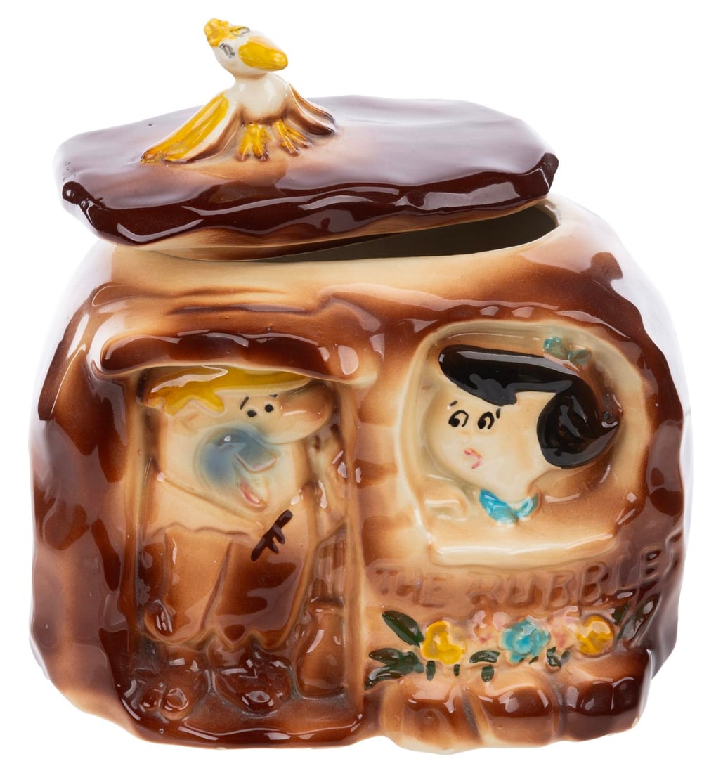 A "The Flintstones" Betty and Barney Cookie Jar.: (Hanna-Barbera, 1960s) A ceramic cookie jar featuring Barney and Betty Rubble in their boulder home from "The Flintstones," with the roof of the house as the jar's lid. Measuring 7" x 10" x 9.75" tall