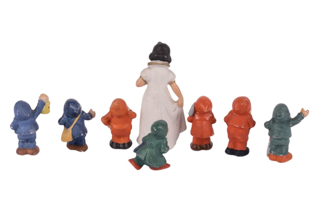 A Snow White and the Seven Dwarfs Ceramic Figurine Set.: (1950s-60s) A set of eight ceramic figurines inspired by "Snow White and the Seven Dwarfs." The Snow White figurine is painted in white and gold, with the number 2470 embossed on the back and the numb