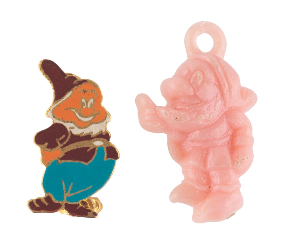 A Pair of "Snow White and the Seven Dwarfs" Souvenirs.: (Disney, 1950s-80s) A pin of Happy and a charm of Grumpy. The "Snow White and the Seven Dwarfs" souvenirs are in very good condition, with wear and spots of paint loss.
