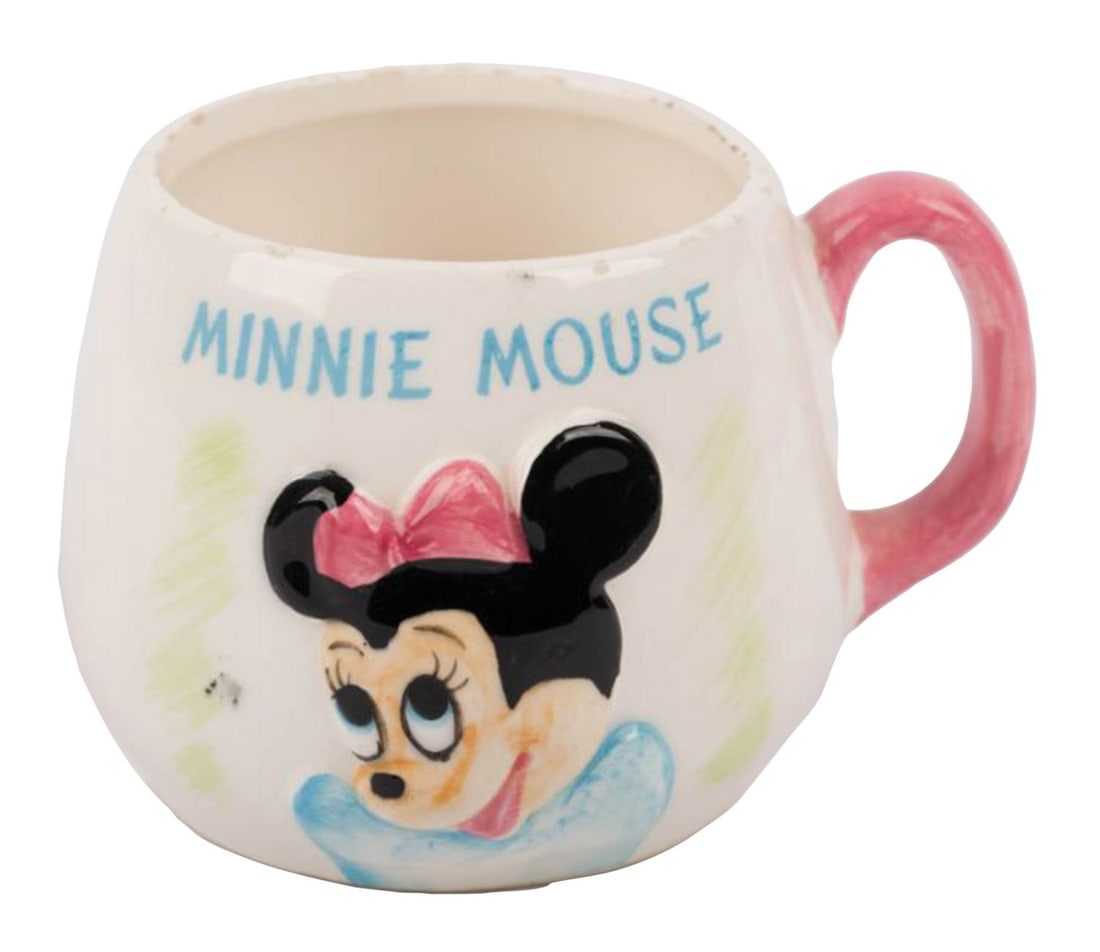 A 1960s Minnie Mouse 3D Mug.: (Enesco, 1960s) A ceramic mug featuring a 3D relief of Minnie Mouse, manufactured by Enesco. Measuring 4" x 5" and 3" tall, the mug is in good condition with small chips along the rim, discoloration a