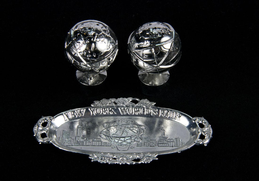 A World's Fair Unisphere Salt & Pepper Shaker Set.: (World's Fair, 1964) A pair of metal Unisphere-themed salt and pepper shakers with a matching tray from the 1964-65 New York World's Fair. Both shakers measure approximately 2" tall, and the tray
