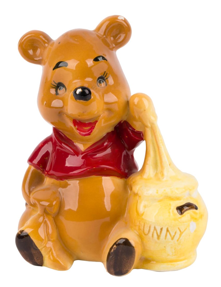 A Winnie the Pooh Ceramic Figurine by Enesco.: (Enesco, 1970s) A ceramic figurine of Winnie the Pooh with a pot of "Hunny," manufactured by Enesco. Measuring 3.5" x 2.5" and 4.25" tall, the figurine is in very good condition with light wear from