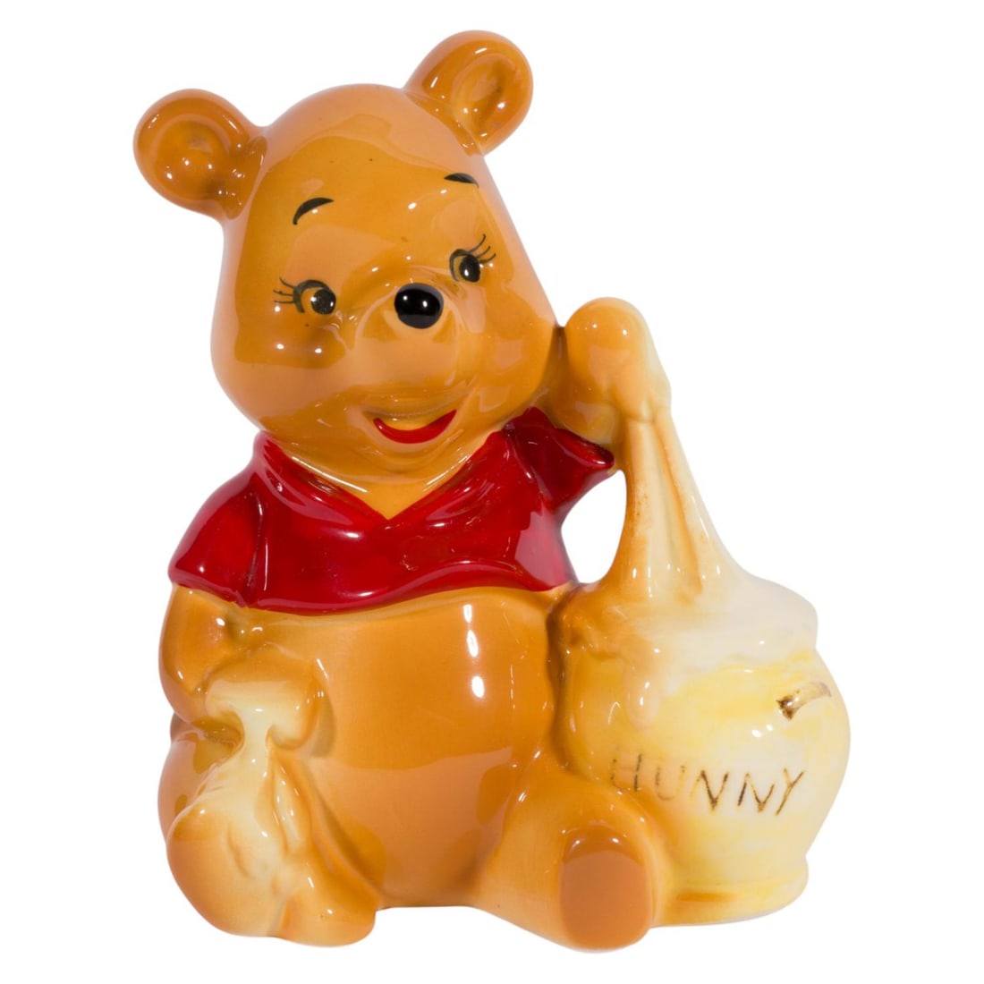 A 1970s Winnie the Pooh Ceramic Figurine.: (Enesco, 1970s) A ceramic figurine of Winnie the Pooh eating from a pot labeled "Hunny," likely sold the Disney Parks in the 1970s. Measuring 3.5" x 2.5" and 4.25" tall, the figurine is in very good