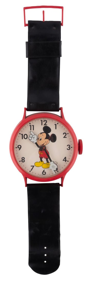 A Giant Mickey Mouse Wristwatch Wall Clock.: (Disney, 1970s) A wall clock designed in the shape of a giant Mickey Mouse wristwatch. Measuring 38" x 9.75", the clock displays in good condition with scuffs to the plastic face, and requiring