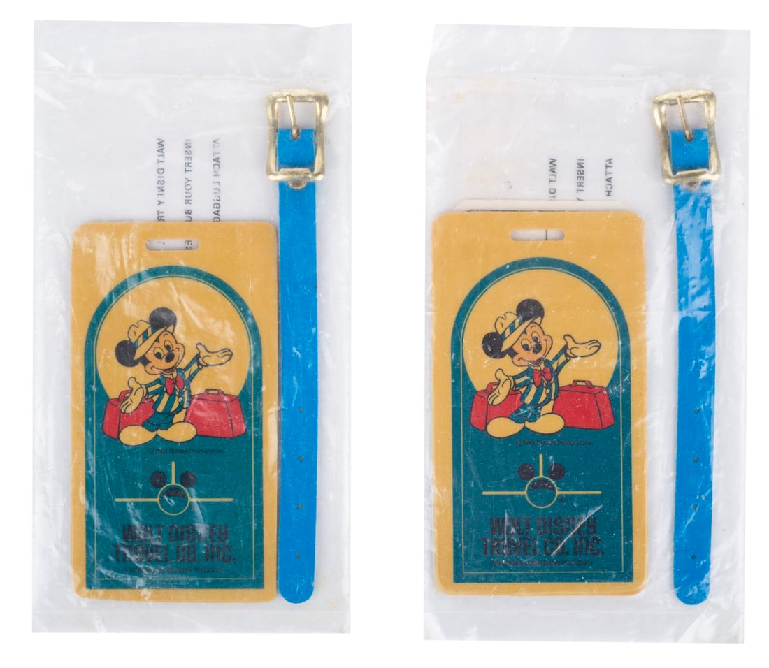 A Pair of Walt Disney Travel Company Luggage Tags.: (Disney, 1987) A pair of Walt Disney Travel Company Mickey Mouse luggage tags, with an ID card and strap. Measuring 2.25" x 4", the unopened tags are in very good condition, showing only handling